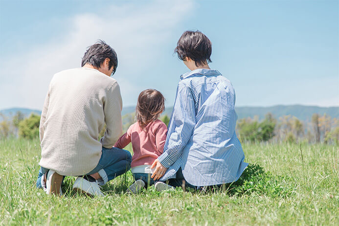 芝生に座って休日を楽しむ親子3人の後ろ姿